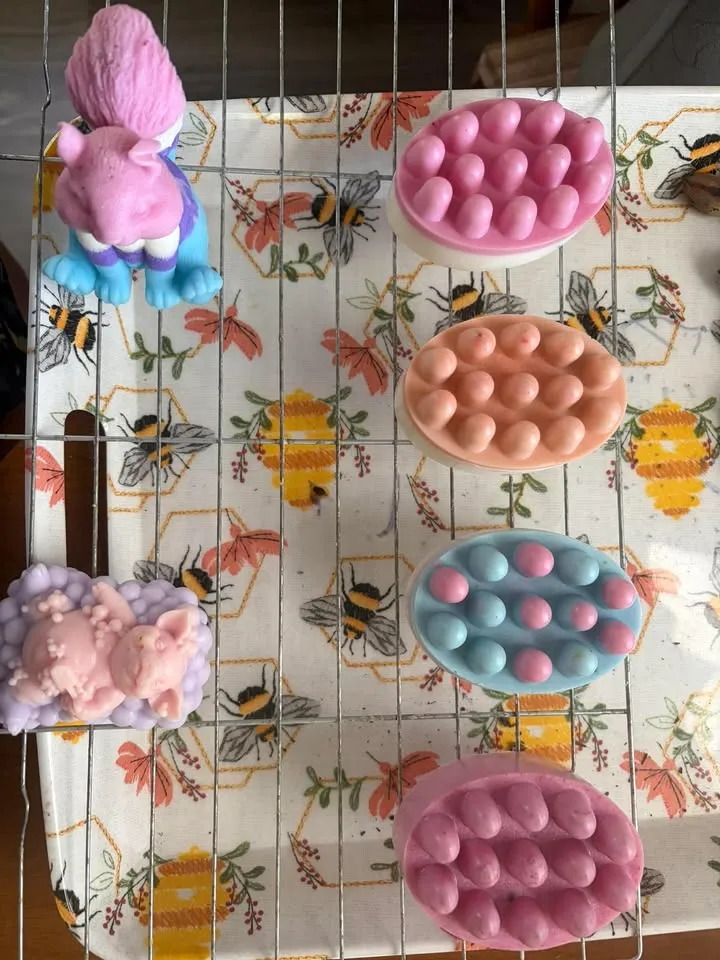 Pink, peach and blue massage bars with a pig soap on Katrinia's bee print tablecloth